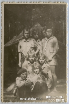 Zdjęcie grupowe młodych harcerzy w mundurach na tle obozowiska w lesie