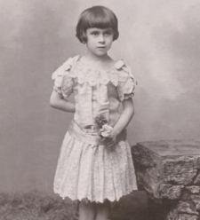 Dziewczynka w koronkowej sukience, skarpetkach, w ręku trzyma kwiaty