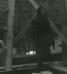 Kobieta ciepło ubrana na rusztowaniach odbudowującego się budynku