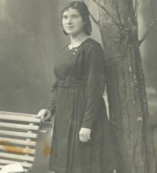 Kobieta w ciemnej sukni i jasnych pantoflach stoi przy ławce w atelier fotograficznym