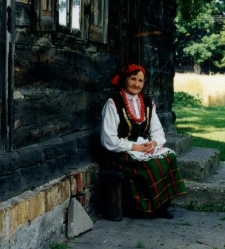 Elżbieta Daniszewska w stroju ludowym siedzi przed drewnianym domem